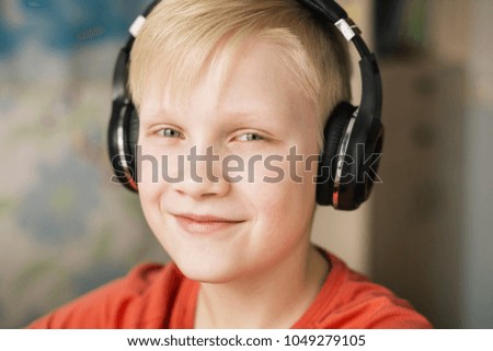 Blond smiling boy listening music in headphones, smiling and looking at camera.