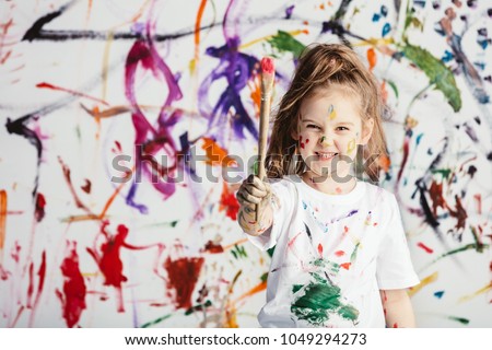 Cute child with smuges of colorful paint showing a paint brush. Little artist. Royalty-Free Stock Photo #1049294273