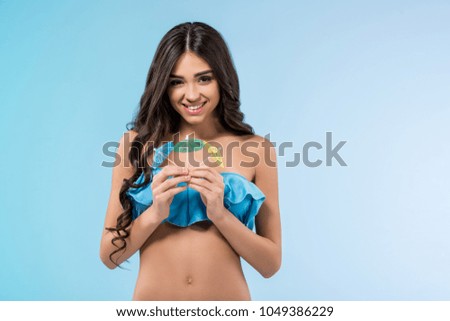 attractive tanned girl in swimsuit holding cocktail umbrellas, isolated on blue