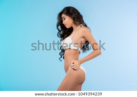 brunette slim girl posing in white swimsuit, isolated on blue