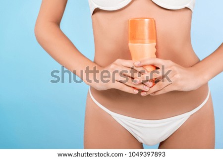 cropped view of slim girl with bottle of sunscreen, isolated on blue