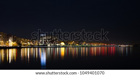 Long exposure of a city bay at night with reflecting lights on water.