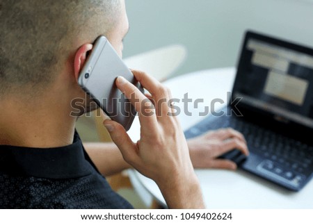 
man speaks on the phone working behind a computer in the interior with white color