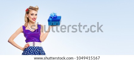 Portrait of smiling woman dressed in pin-up style dress with polka dot, with copyspace area for slogan or advertising text message, on blue background. Blond model in retro fashion and vintage concept