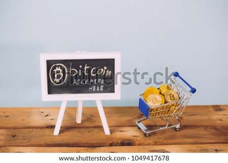 Virtual currency Bitcoin accepted here sign and shopping cart full of bitcoin coins on wooden platform over pastel blue background
