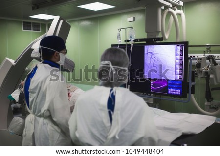 Doctors conduct a diagnostic operation. Coronarography. Percutaneous coronary intervention-recanalization, balloon angioplasty and stenting of the left coronary artery Royalty-Free Stock Photo #1049448404