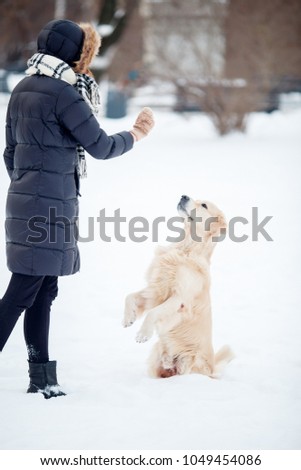 Photo of young woman in black jacket playing with dog in snowy park