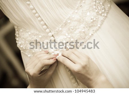 Detail of bridesmaid fixing bride's wedding dress