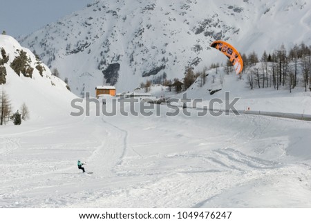 woman who practices snowkiting, snowkite, extreme sport, slides on the snow, pulled by the kite, thanks to the strong wind, high mountains, winter, Simplon Pass, Switzerland Royalty-Free Stock Photo #1049476247