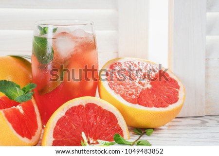 Fresh grapefruits and glass of grapefruit juice with ice and mint on rustic white wooden table opposite the blinds with copy space.  Close-up. Royalty-Free Stock Photo #1049483852