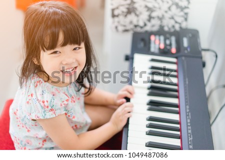 Beautiful little asian girl looking up and playing piano in living room or music school.Kindergarten child having fun with learning to play music instrument.Education, skills concept.