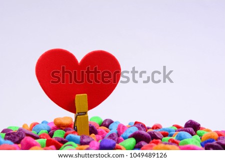 Red color love shape with yellow wooden clip on a colourful candy stones. White background.
