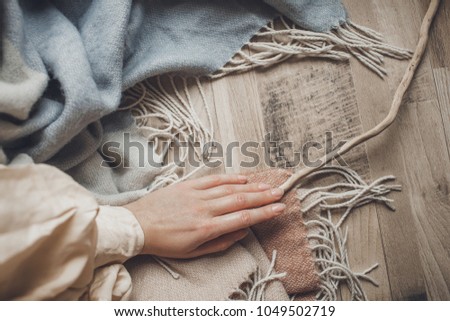 pastel colors tender woman's hand in gently holds a wool blue scarf and branch that lies on a wooden background
