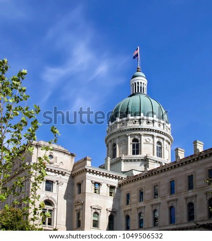 Downtown Indianapolis, Indiana state capital building on a blue sunny day with American flag flying.