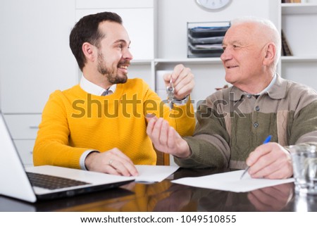 Elderly man and young agent sign lease contract of apartment at office and hand over keys