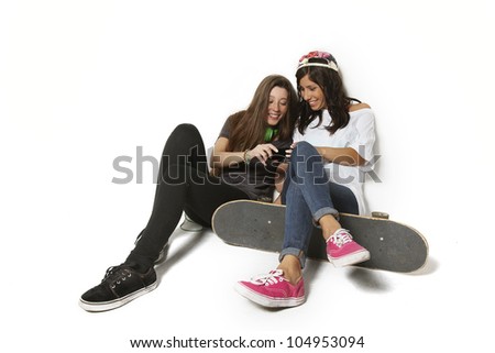 Two young  skateboarding girl friends looking at pictures on phone- isolated over white background.