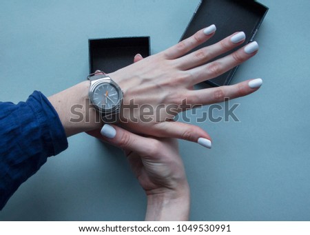 Womans hands dress grey watchs on her wrist. Flat lay. Top view. Space for text. Black gift box. Grey background. Expensive present.
