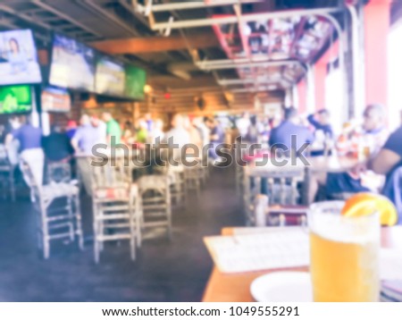 Blurred sports bars and restaurants in USA. Big Ale beer mug with orange slice, large wall mount flat-screen TV, classic wooden table, chair. People drink craft beer, hanging out, watching sport
