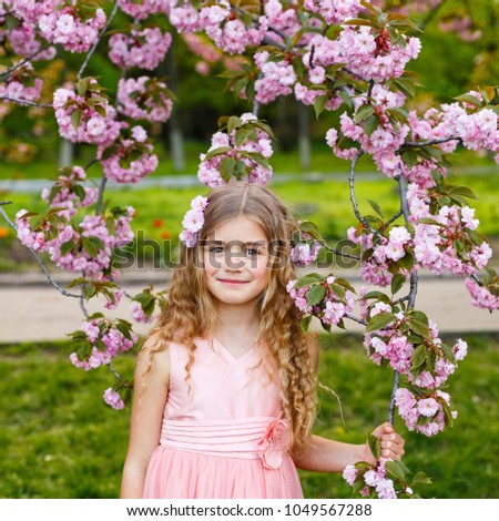 Pretty little girl in blossom cherry garden in sunny spring day