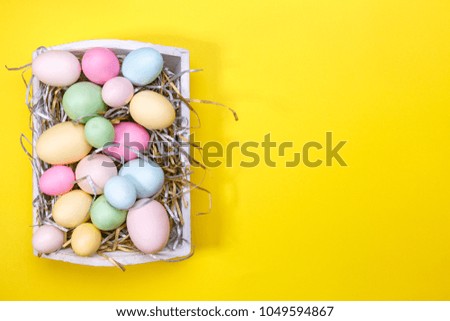 Multicolor eggs in a white tray. Creative Easter concept. Modern solid yellow background. Horizontal