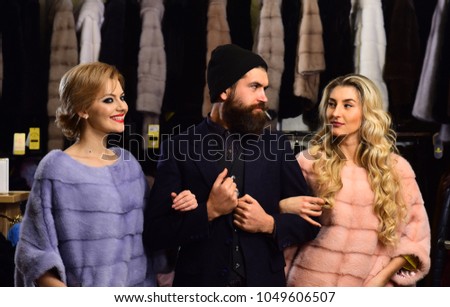 Women in violet and pink fur coats with male shop assistant. 