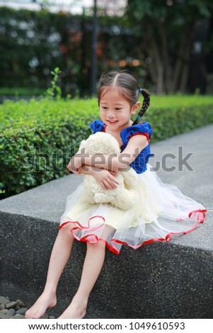Adorable little Asian girl dressed with a fantasy outfit sitting in the garden with teddy bear.