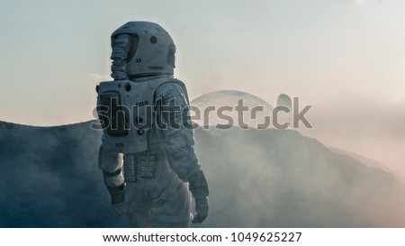 Shot of the Astronaut on Red Planet Watching Toward His Base/Research Station. Near Future First Manned Mission To Mars, Technological Advance Brings Space Exploration, Colonization. Royalty-Free Stock Photo #1049625227