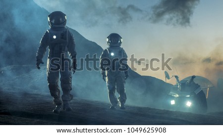 Two Astronauts in Space Suits Confidently Walking on Alien Planet, Exploration of the the Planet's Surface. In the Background Research Base/ Station and Rover. Space Travel, Colonization Concept. Royalty-Free Stock Photo #1049625908