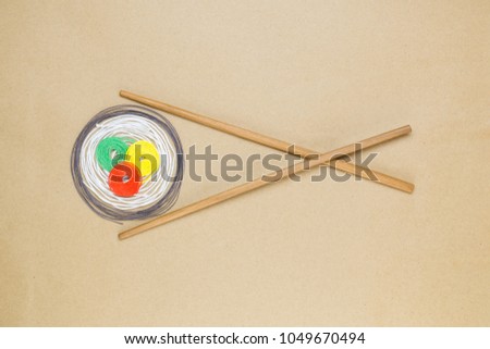 Sushi roll made of colorful threads with chopsticks isolated on beige background minimal flat lay creative concept