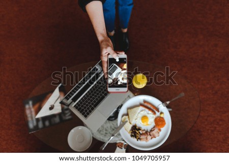 girl takes pictures of her breakfast at the hotel with a laptop and juice on her smartphone
