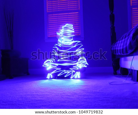 A long exposure picture of a person sitting on the floor illuminated by a drawn silhouette in blue.