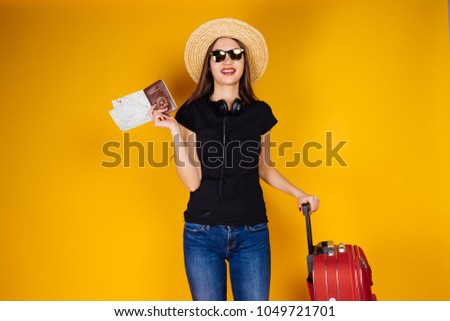 a smiling young girl in sunglasses and a hat goes on a trip, with a suitcase, holds tickets for the plane