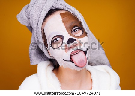 young girl with a towel on her head, on her face a mask with a picture of a muzzle of a dog, shows a tongue