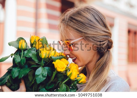 Side view of cheerful gorgeous woman in sunglasses, sniffs yellow roses, outside. Summertime