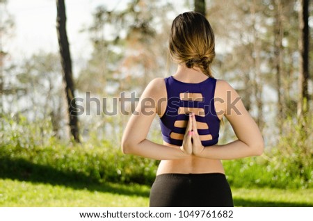 young woman from behind doing yoga pose outdoors in park