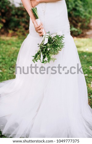 close-up of a bride's hand with a bouquet in a white dress which is flipped back and stands on a meadow