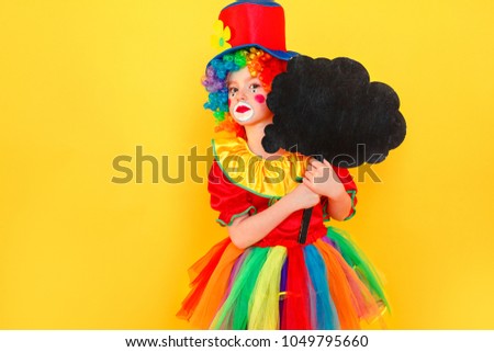 Unhappy girl in clown costume and hat holding black table