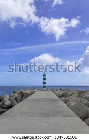 Lighthouse on the end of the pier under the blue cloudy sky on a sunny day