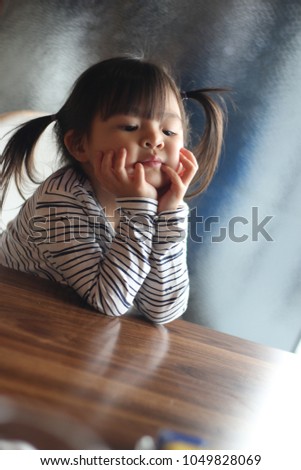 A lovely Chinese little girl is using her hands to touch her face while she is looking down and day dreaming, Tuen Mun, New Territories, Hong Kong, Soft Focus