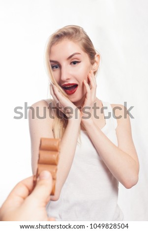 health, people, food and beauty concept - Lovely smiling teenage girl eating chocolate. girl is surprised by the chocolate. man's hand with chocolate