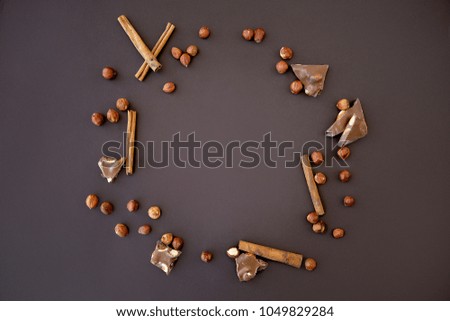 composition with hazelnuts, pieces of chocolate and cinnamon lined in a circle on a dark brown background