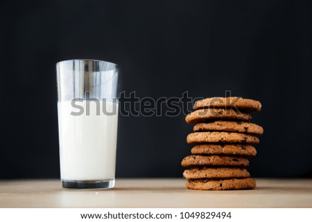 close-up of a cookie with chocolate and a glass of milk on a wooden table on a black background