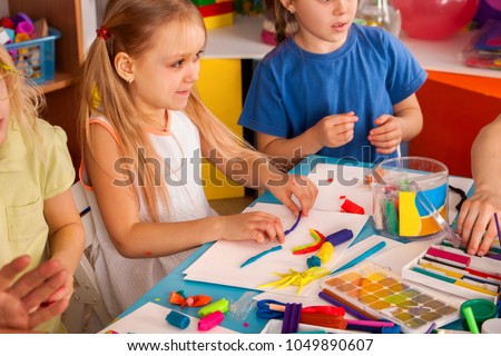 Plasticine modeling clay in children class. Teacher teaches kids together play dough and mold from plasticine in kindergarten or preschool. Group of four people. School exhibition.