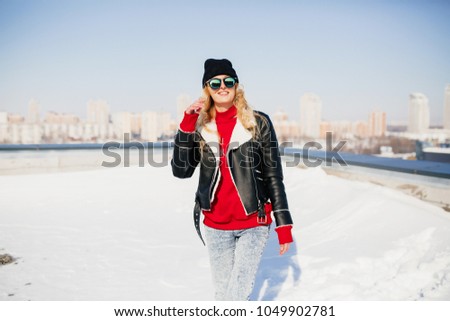 Portrait of fashionable blonde girl dressed in red pullover and jeans against the background of city. outdoor photo of young hipster woman in the city