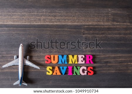 Conceptual image of SUMMER SAVING text and miniature plane on wooden table top