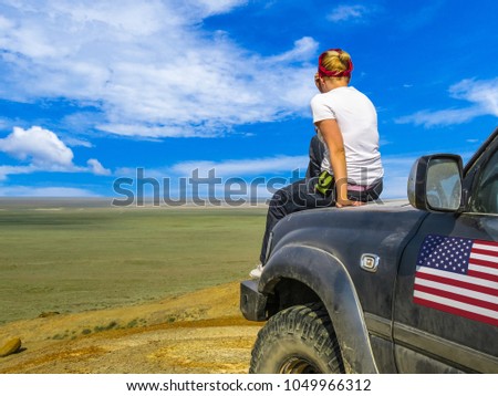 Young girl sitting back on the hood of a big car suv. Off-road travel America, USA background. Desert