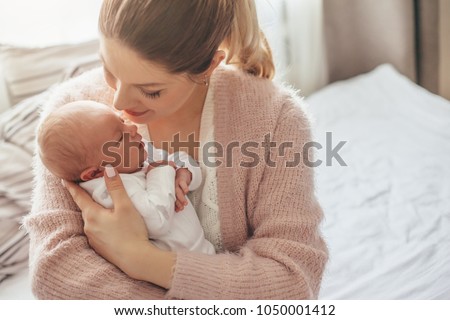 Home portrait of a newborn baby with mother on the bed. Mom holding and kissing her child. Royalty-Free Stock Photo #1050001412