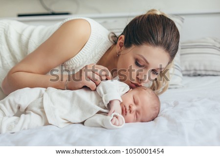 Home portrait of a newborn baby with mother on the bed. Mom kissing her sleeping child.