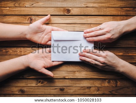 Hands pass the white envelope to the other hands on a wooden background. Transfer of money for donation. To send a letter.