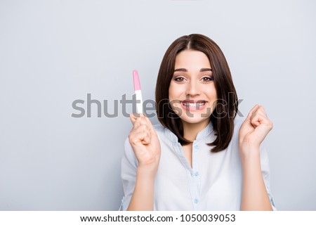 Yes, I am pregnant! Portrait of attractive charming pretty brunette surprised glad woman demonstrating positive result on pink and white test stick isolated on grey background Royalty-Free Stock Photo #1050039053